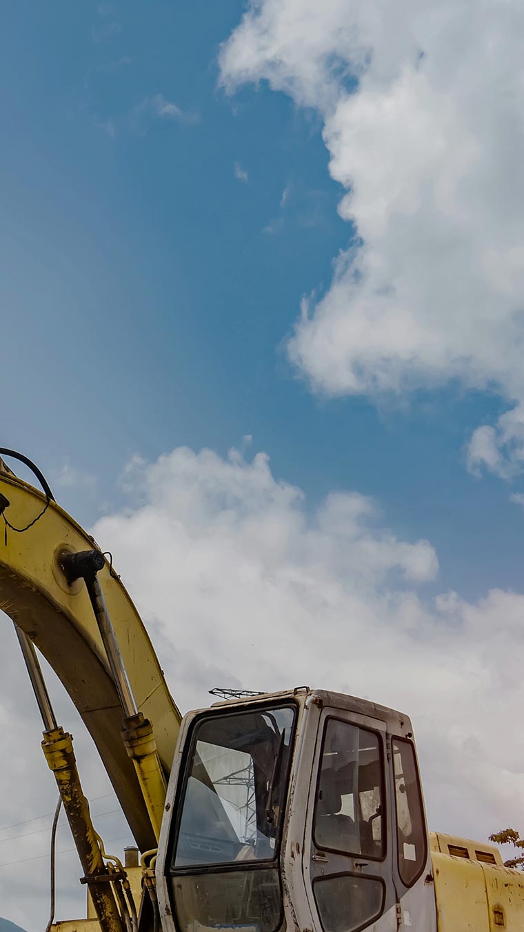 Pelleteuse jaune de chantier en activité sur un terrain déblayé sous un ciel bleu clair sans nuages, avec des traces de travaux visibles au sol