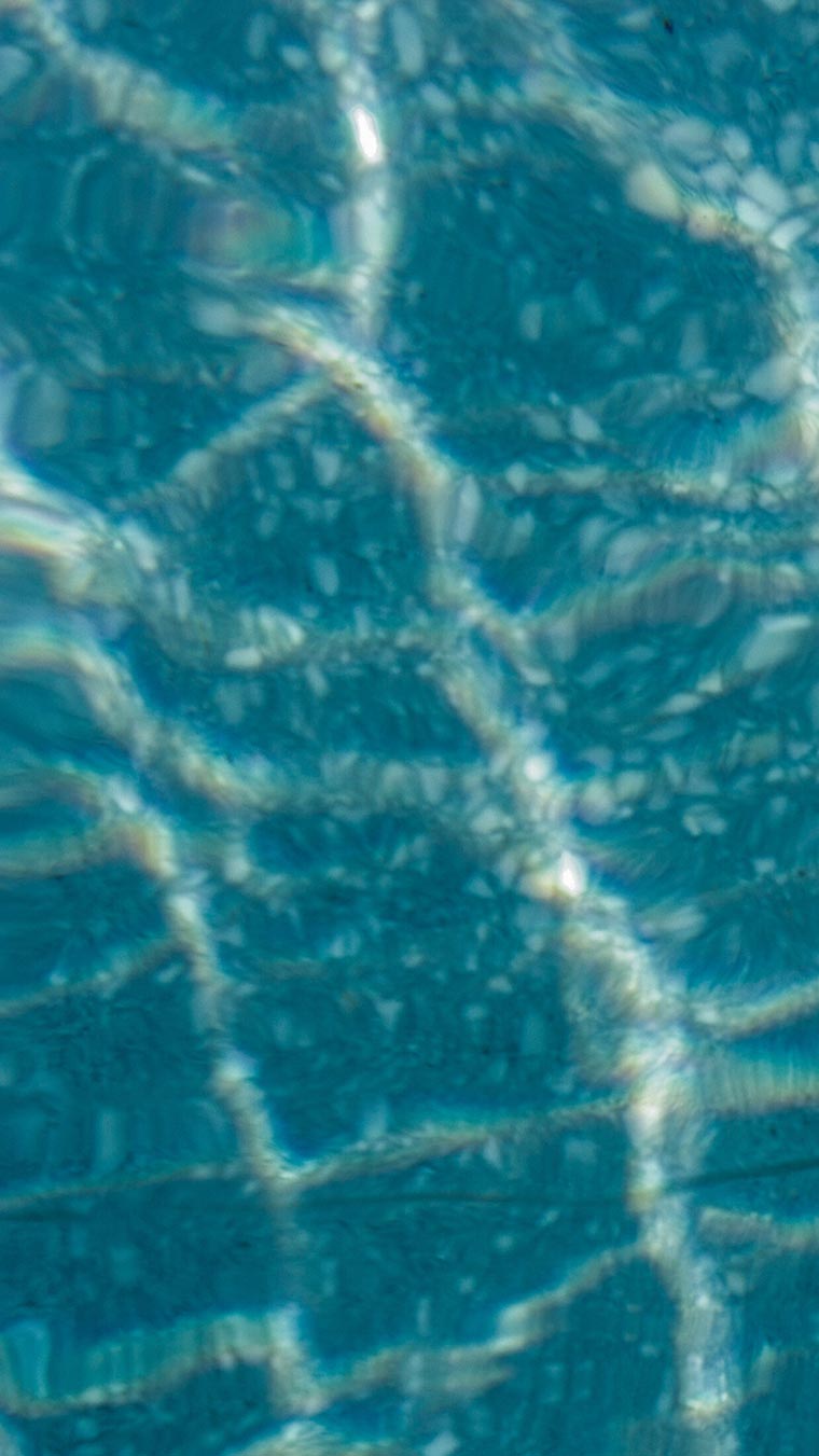 Eau cristalline et limpide de la piscine du camping sous un ciel lumineux, avec reflet éclatant à la surface et ambiance paisible propice à la détente en plein air