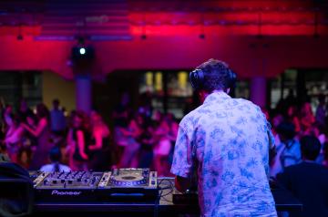 Soirée DJ set animée en plein air au camping en bord de mer dans les Landes, avec un DJ professionnel aux platines, des jeux de lumière colorés, et un public de vacanciers dansant joyeusement sous un ciel étoilé, dans une ambiance festive et conviviale.