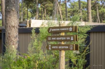 Panneau en bois de signalisation au camping Le Vieux Port dans les Landes, indiquant les différents points d’intérêts du site tels que le parc aquatique, les terrains multisports, les commerces et restaurants, situé sous les pins dans un cadre naturel en bord de mer, facilitant l’orientation des campeurs dans cet espace vaste et arboré.