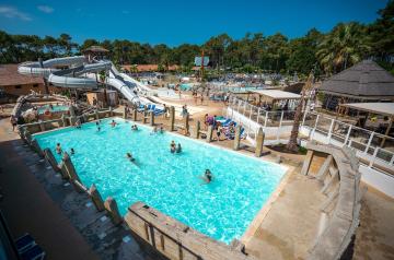 Vue panoramique de la grande piscine extérieure du parc aquatique XXL du camping Le Vieux Port dans les Landes, avec un bassin spacieux et tempéré accueillant des cours de natation, des compétitions de water-polo, et diverses activités aquatiques, entouré de palmiers et de toboggans colorés, dans un environnement familial et convivial au cœur d’une pinède en bord de mer.