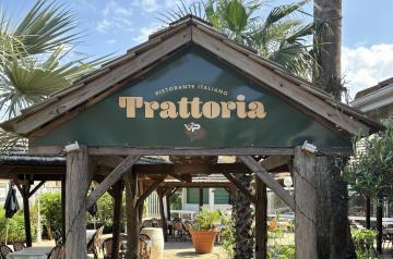 Intérieur chaleureux et convivial de la Trattoria, restaurant italien du camping Le Vieux Port dans les Landes, avec sa décoration typique mêlant bois et éclairage doux, des tables élégamment dressées accueillant des vacanciers dégustant des spécialités italiennes comme des pâtes fraîches et des pizzas, dans une ambiance festive et familiale proche du parc aquatique.