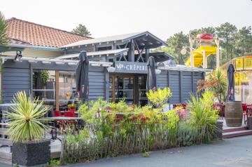 Intérieur chaleureux et convivial de la Crêperie du camping Le Vieux Port dans les Landes, avec des vacanciers installés à des tables en bois dégustant des galettes et crêpes bretonnes salées et sucrées, servis par un personnel souriant dans une ambiance familiale et détendue, avec une décoration simple et authentique rappelant la Bretagne.