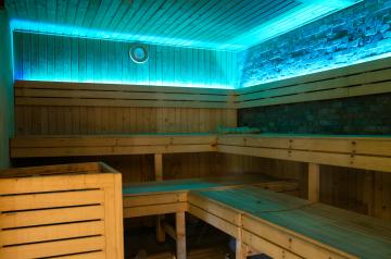 Intérieur du sauna du camping Le Vieux Port, avec des bancs en bois clair disposés en gradins, un poêle chauffant diffusant une chaleur agréable, et une atmosphère tamisée propice à la détente. L’espace bien-être du camping inclut également un hammam et des soins du corps, offrant aux vacanciers un lieu apaisant pour se relaxer après une journée au parc aquatique ou à la plage, dans un cadre naturel et élégant typique des Landes.