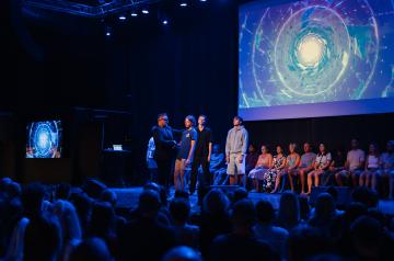 Spectacle d’hypnose et de mentalisme à l’Arena du camping Le Vieux Port, avec Magic Chaz sur scène, hypnotiseur renommé captivant le public dans un show à la fois drôle, bluffant et mystérieux. Les participants, invités sur scène, sont plongés dans un état de conscience modifié, vivant des expériences fascinantes sous des jeux de lumière et une ambiance théâtrale, tandis que le public rit et s’émerveille des phénomènes hypnotiques et des performances de mentalisme orchestrées avec respect et sécurité.