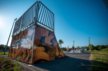 Skatepark du camping équipé de modules variés, notamment des rampes, des mini-ramps, des bowls, des modules de glisse, des ledges, et des figures de saut. Sur la scène, des skateurs en action, utilisant des surfaces en béton, en asphalte ou en matériaux modulaires comme l’aluminium et le bois, évoluent avec dynamisme. Le terrain, aménagé en espace convivial et sécurisé, comporte également des équipements complémentaires tels que des bancs et poubelles, pour accueillir aussi bien débutants que bons skateurs.