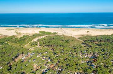 Vue panoramique aérienne prise par drone du camping, montrant les emplacements verts et les structures du camping en premier plan, avec un vaste horizon bleu de l’océan Atlantique s’étendant à l’arrière-plan sous un ciel clair et lumineux