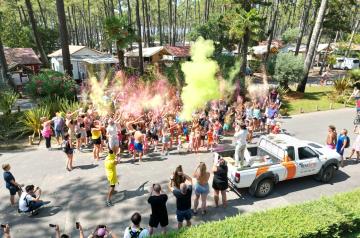 Participants vêtus de blanc lancent en l'air des nuages de poudre colorée vive au cours d'une animation Color Run en extérieur. Des nuages multicolores de jaune, rose, bleu, vert et orange s'entremêlent dans l'air, créant une ambiance festive et dynamique. Les participants souriants, les bras levés, sont engagés dans cet instant de joie collective et de partage, symbolisant l'esprit ludique et de cohésion de cet événement sportif non compétitif où la couleur est reine.