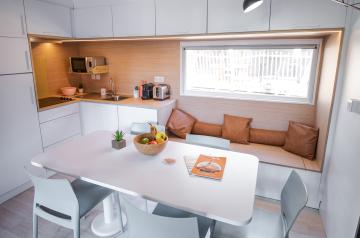 Intérieur lumineux et cosy d'un locatif blanc, présentant un salon avec des murs immaculés et une décoration minimaliste mais chaleureuse. Le mobilier, aux teintes claires, comprend un canapé confortable, des coussins doux et un tapis beige qui apportent une ambiance accueillante. La lumière naturelle filtre par une grande fenêtre, mettant en valeur l'atmosphère paisible et soignée de cet espace convivial et élégant.