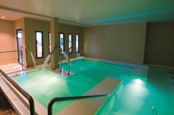 Espace aquatique intérieur d’un spa moderne avec bassins d’eau claire, mettant en avant plusieurs bras de jets d’eau puissants et orientables projetant des cascades d’eau apaisantes, créant une ambiance relaxante dans un cadre lumineux et épuré