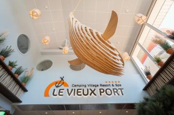 Gros plan baleine en bois suspendue réception camping : sculpture décorative thème marin, design artisanal, détail artistique ambiance cocooning et nature au port de vacances.