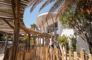 Entrée de la réception du camping rénovée : vue sur les bureaux hôtesses, bornes check-in, grand logo, banc végétal et baleine en bois suspendue, accueil moderne et design.