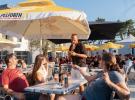 Jeu SOL'APERO avec un animateur qui pose des questions aux résidents lors de leur pause de fin de journée ensoleillée avec les parasols jaunes de la marque Pelforth