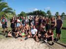 Photo de groupe montrant une dizaine d'adolescents souriants et détendus, posant ensemble sur la terrasse de la plaine des sports au camping, avec des arbres et des installations sportives en arrière-plan, lors d'une activité ou d'une sortie organisée au sein du club ados