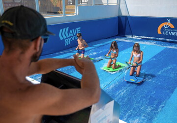 Camping avec simulateur de vagues en bord de mer dans les Landes machine à surf bouées tractées le surf et le bodyboard le kneeboard une vague douce ou pentue - enfants s'amusant à la surface de l'eau avec maître nageur réserver un séjour camping à prix réduit
