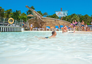 Enfant s'amusant gaiement dans l'eau chauffée de la pataugeoire du parc aquatique du camping 5 étoiles dans les Landes en bord de mer