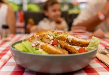 flou d'une famille à table avec au 1er plan une salade césar très joliment préparée à la brasserie VP du camping avec restaurants des Landes 5 étoiles