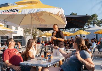 Jeu SOL'APERO avec un animateur qui pose des questions aux résidents lors de leur pause de fin de journée ensoleillée avec les parasols jaunes de la marque Pelforth