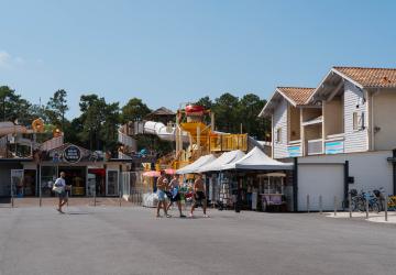 Commerces-services-camping-5-etoiles-vieux-port-landes-boutiques-velos-pour-acheter-tous-les-objets-de-plage-et-autres-souvenirs-de-vacances-dans-les-landes-en-bord-de-mer-avec-des-jeunes-personnes-qui-marchent-sur-la-place-du-village-vers-leur-location-de-vélos