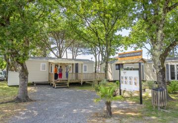 Visite guidée d’un mobil-home moderne sur un camping familial, montrant l’intérieur lumineux avec salon, cuisine et terrasse extérieure en bois, destinée aux futurs propriétaires souhaitant investir dans une résidence de vacances