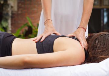Séance de massage réalisée par un ostéopathe professionnel sur une femme en tenue de sport, allongée sur une table de soin, dans l’espace bien-être du meilleur camping des Landes en bord de mer, avec en arrière-plan une atmosphère relaxante ouverte sur la nature.
