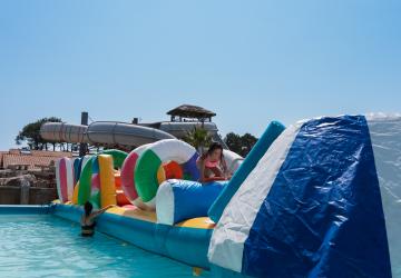 Animation de jeu aquatique Total Wipe Out pour les enfants et adolescents au camping Le Vieux Port à Messanges, comprenant une grande aire avec des obstacles gonflables flottants, des ponts suspendus, des trampolines, et des bouées, offrant une activité ludique, sportive et rafraîchissante en plein air sous un ciel ensoleillé