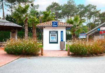 Distributeur automatique de billets Euronet flambant neuf, installé à l’entrée du camping, identifiable par son habillage aux couleurs bleues et jaunes. Le DAB est accessible en libre-service à proximité des installations du camping, permettant aux vacanciers de retirer de l’argent liquide facilement durant leur séjour. 