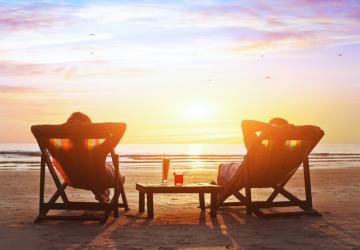 Coucher de soleil aux couleurs rose et doré sur une plage des Landes, avec deux transats installés sur le sable. Deux personnes assises confortablement, profitant d'un moment de détente en mode chill face à l'océan, sous un ciel aux teintes douces et lumineuses, avec des dunes et une végétation naturelle en arrière-plan.