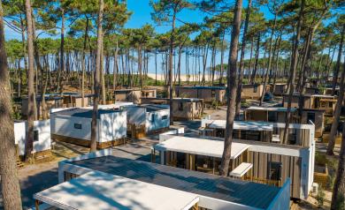 All-inclusive-services-camping-5-etoiles-vieux-port-landes-quartier-premium-vue drone du haut des toits des mobil homes par beau temps ensoleillé avec la pinède et la vue sur la dune derrière l'océan