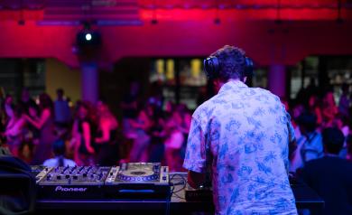 Soirée DJ set animée en plein air au camping en bord de mer dans les Landes, avec un DJ professionnel aux platines, des jeux de lumière colorés, et un public de vacanciers dansant joyeusement sous un ciel étoilé, dans une ambiance festive et conviviale.