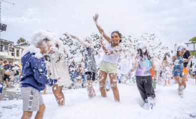 Soirée mousse dans un camping avec plusieurs enfants souriants et jouant ensemble au milieu des bulles de mousse, ambiance festive et joyeuse en plein air.