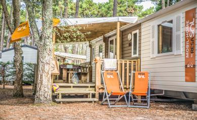 Mobil home moderne vu de près au camping Le Vieux Port dans les Landes, avec une grande terrasse en bois équipée de chaises longues confortables, entouré de pins majestueux typiques de la pinède landaise, offrant un cadre paisible et ombragé à quelques pas de la plage en bord de mer.