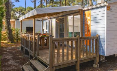 Terrasse en bois spacieuse d’un mobil home moderne situé sous les pins au camping Le Vieux Port dans les Landes, avec chaises longues pour se détendre, vue sur la végétation dense de la pinède landaise et accès direct à l’extérieur, offrant un cadre naturel et paisible en bord de mer, idéal pour des vacances reposantes en famille ou entre amis.