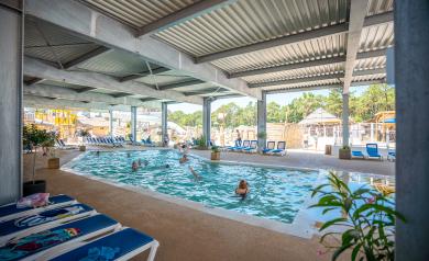 Grande piscine couverte et chauffée à 28°C du parc aquatique du camping 5 étoiles Le Vieux Port dans les Landes, entourée d’une structure moderne avec de larges ouvertures laissant entrer la lumière naturelle et facilitant les accès rapides, offrant un espace de baignade calme et convivial adapté à tous les âges, avec des zones de détente et des équipements de qualité pour profiter de la baignade en toute saison.