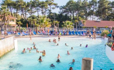 Grande piscine à vagues lagon du parc aquatique du camping Le Vieux Port dans les Landes, avec des eaux turquoise légèrement agitées créant jusqu’à 7 niveaux de vagues pour le plaisir des nageurs de tous âges, entourée d’un décor naturel de palmiers et pinède, offrant une expérience ludique proche de l’océan dans un espace sécurisé et convivial pour toute la famille.