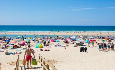 Personne marchant sur un chemin sécurisé reliant le camping Le Vieux Port dans les Landes à la plage de l’océan Atlantique, portant un sac Resasol, entourée de dunes et de pins de la pinède landaise, profitant d’un accès direct et facile à la plage depuis ce camping 5 étoiles avec tout le confort en bord de mer, sous un ciel lumineux et dégagé.