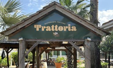 Intérieur chaleureux et convivial de la Trattoria, restaurant italien du camping Le Vieux Port dans les Landes, avec sa décoration typique mêlant bois et éclairage doux, des tables élégamment dressées accueillant des vacanciers dégustant des spécialités italiennes comme des pâtes fraîches et des pizzas, dans une ambiance festive et familiale proche du parc aquatique.