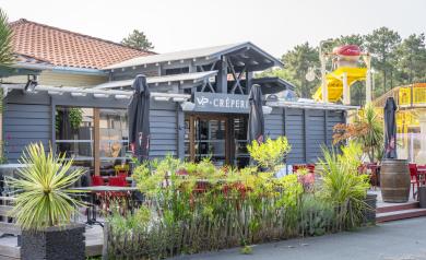 Intérieur chaleureux et convivial de la Crêperie du camping Le Vieux Port dans les Landes, avec des vacanciers installés à des tables en bois dégustant des galettes et crêpes bretonnes salées et sucrées, servis par un personnel souriant dans une ambiance familiale et détendue, avec une décoration simple et authentique rappelant la Bretagne.