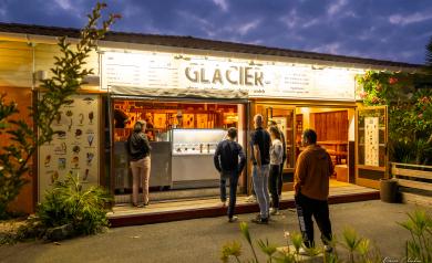 Glacier du camping Le Vieux Port ouvert la nuit, éclairé par des lumières chaleureuses qui attirent les vacanciers désireux de savourer des glaces artisanales et des desserts sucrés. Le stand est animé par un personnel souriant, avec une ambiance festive et conviviale sous un ciel étoilé, offrant un moment de détente gourmand en fin de journée dans ce camping 5 étoiles en bord de l’océan Atlantique.