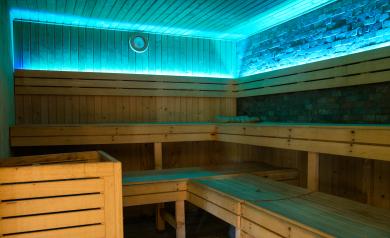 Intérieur du sauna du camping Le Vieux Port, avec des bancs en bois clair disposés en gradins, un poêle chauffant diffusant une chaleur agréable, et une atmosphère tamisée propice à la détente. L’espace bien-être du camping inclut également un hammam et des soins du corps, offrant aux vacanciers un lieu apaisant pour se relaxer après une journée au parc aquatique ou à la plage, dans un cadre naturel et élégant typique des Landes.