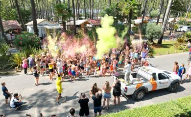 Participants vêtus de blanc lancent en l'air des nuages de poudre colorée vive au cours d'une animation Color Run en extérieur. Des nuages multicolores de jaune, rose, bleu, vert et orange s'entremêlent dans l'air, créant une ambiance festive et dynamique. Les participants souriants, les bras levés, sont engagés dans cet instant de joie collective et de partage, symbolisant l'esprit ludique et de cohésion de cet événement sportif non compétitif où la couleur est reine.