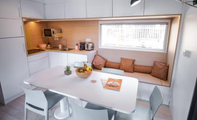 Intérieur lumineux et cosy d'un locatif blanc, présentant un salon avec des murs immaculés et une décoration minimaliste mais chaleureuse. Le mobilier, aux teintes claires, comprend un canapé confortable, des coussins doux et un tapis beige qui apportent une ambiance accueillante. La lumière naturelle filtre par une grande fenêtre, mettant en valeur l'atmosphère paisible et soignée de cet espace convivial et élégant.