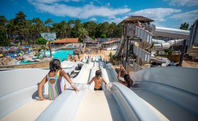 Trois enfants heureux descendant en même temps un grand toboggan coloré dans un parc de jeux en plein air, leurs visages rayonnants de joie et d’excitation alors qu’ils glissent rapidement vers le bas sous un ciel ensoleillé