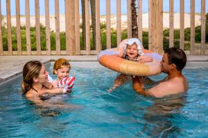famille heterosexuelle heureuse avec un enfant et un bébé dans la piscine de leur logement premium du camping des Landes avec vue sur la dune pendant une juornée enseillée au ciel bleu