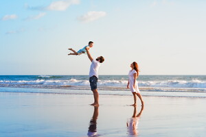 famille heureuse à la plage à marée basse avec l'enfant jeté dans les bras du papa et la maman derrière miroir d'eau BLOG Le Vieux Port article 2025 Découvrez la Wishlist la nouvelle fonctionnalité du camping 5 Le Vieux Port La magie des vacances de Noël et des fête de fin d'année sauvegarder séjour camping