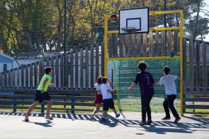 Camping avec City Stade dans les Landes en bord de mer (3) jeunes enfants en train de jouer au basket dans la safe place du terrain multisport avec le ballon qui va passer dans le panier