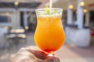 Cocktail orange avec un fond de grenade, une paille, tenu dans la main d'un homme avec un flou artistique en arrière-plan
