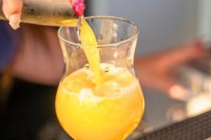 camping avec bars et restaurants avec une main féminine manucurée en rose et transparent avec des fleurs en train de remplir un verre à cocktail avec jus d'orange frais