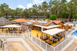 vue en hauteur depuis le solarium du restaurant-snack-bar le Captain-Mary avec beaucoup de personnes à table en train de se restaurer entre piscines et la machine à surf pendant leur séjour landais