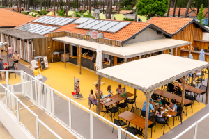 Terrasse du restaurant-bar-snack-lounge du camping des Landes, avec tables alignées et vue sur le parc aquatique avec ses toboggans près de l'océan atlantique